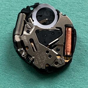 May include: Close-up of a watch movement with intricate mechanical components. The movement features silver, copper, and black elements, including a coil, gears, and the text "NO JEWELS SEIKO TIME CORP 7N83D JAPAN".