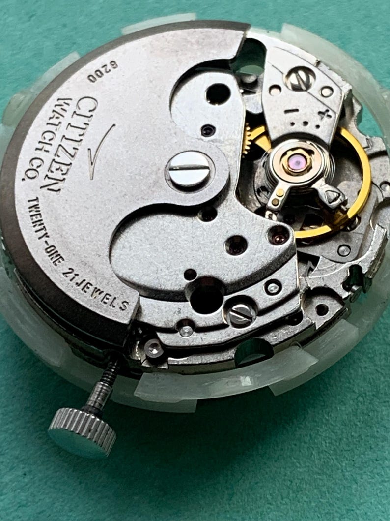 May include: Close-up of a Citizen watch movement, showcasing intricate mechanical components. The silver-toned mechanism features gears, jewels, and the text "Citizen Watch Co. Twenty-One 21 Jewels". A silver crown is visible.