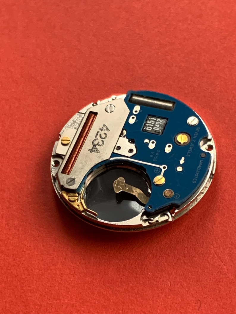 May include: Close-up of a watch movement with a blue circuit board and silver metal components. The watch movement has the number 4234 printed on it. The words "SWISS" and "SEVEN 7 JEWELS" are also visible.