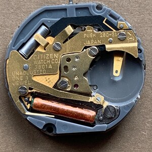 May include: A close-up of a Citizen watch movement, model 3601A, with gold-colored gears and a copper-colored coil. The watch mechanism is gray and has the text "PUSH 280-31 JAPAN" and "ONE 1 JEWEL".