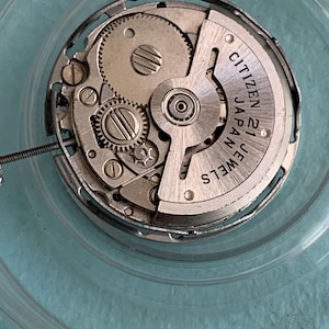 May include: Close-up of a Citizen watch movement with visible gears, screws, and the text "Citizen Japan 21 Jewels". The mechanical components are silver-toned, set against a clear, circular background.