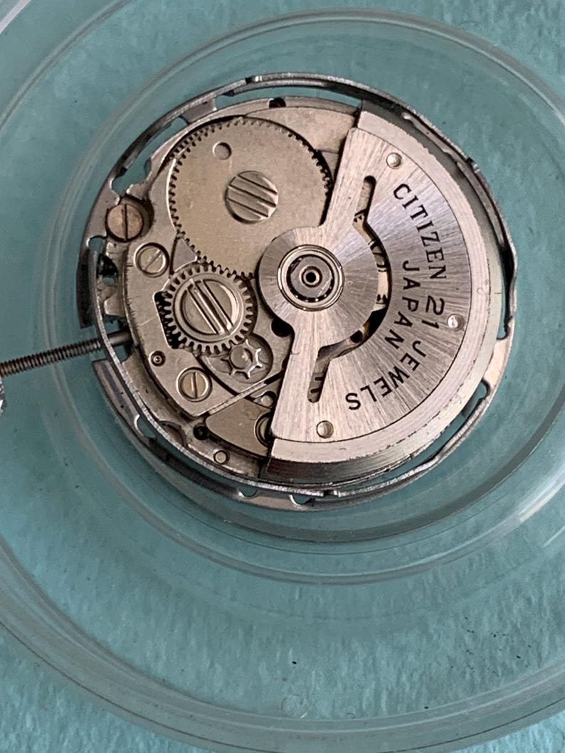 May include: Close-up of a Citizen watch movement with visible gears, screws, and the text "Citizen Japan 21 Jewels". The mechanical components are silver-toned, set against a clear, circular background.