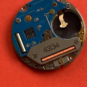 May include: A close-up of a watch movement with a blue circuit board and silver metal components. The text "SEVEN 7 JEWELS" and "SWISS V8" are visible. The number "4234" is printed on the metal.