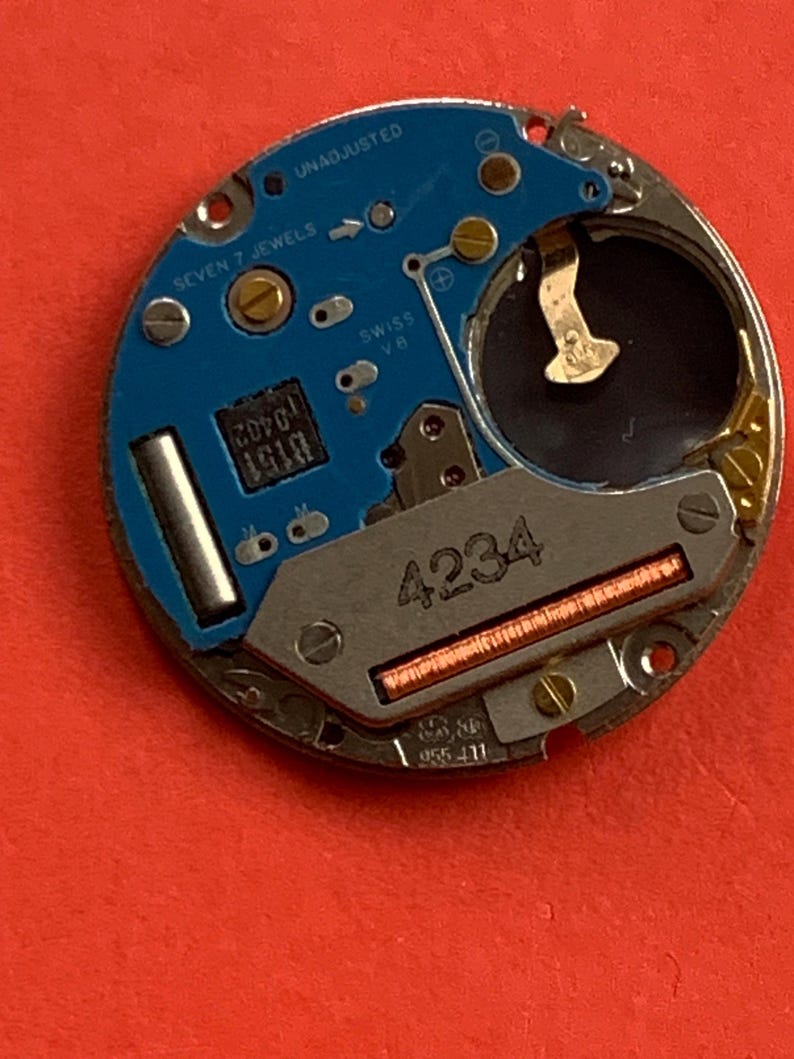 May include: A close-up of a watch movement with a blue circuit board and silver metal components. The text "SEVEN 7 JEWELS" and "SWISS V8" are visible. The number "4234" is printed on the metal.