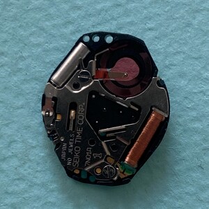 May include: A detailed view of a Seiko watch movement, showcasing its internal mechanisms. The movement is predominantly black, with silver and copper-toned elements. The text "SEIKO TIME CORP" and "JAPAN NO JEWELS" are printed on the movement.