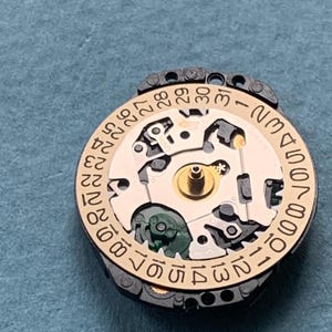 K&ouml;nnte beinhalten: Nahaufnahme eines Uhrwerks mit goldfarbenem Zifferblatt und schwarzem Au&szlig;enring. Das Zifferblatt zeigt das Datum von 1 bis 31 an. Die komplizierten Innenarbeiten der Uhr sind sichtbar.