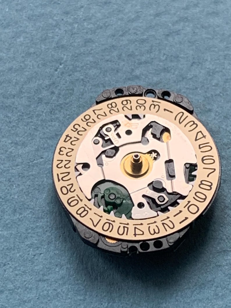 K&ouml;nnte beinhalten: Nahaufnahme eines Uhrwerks mit goldfarbenem Zifferblatt und schwarzem Au&szlig;enring. Das Zifferblatt zeigt das Datum von 1 bis 31 an. Die komplizierten Innenarbeiten der Uhr sind sichtbar.