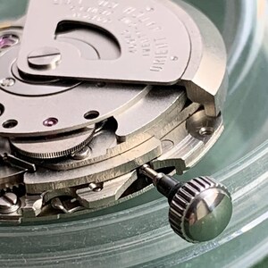 May include: Detailed view of a mechanical watch movement, revealing complex gears and mechanisms. The silver metal components are finely crafted, with a visible winding crown. The watch is marked with "ORIENT" and "JAPAN".