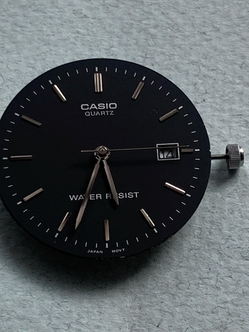 Puede incluir: Esfera de reloj Casio Quartz negra con agujas e indicadores dorados. La esfera muestra "CASIO QUARTZ" y "WATER RESIST". Ventana de fecha a las 3. Corona plateada.