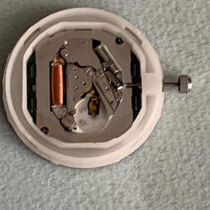 Puede incluir: Un movimiento de reloj con una carcasa de pl&aacute;stico blanco. Los componentes internos incluyen una bobina de color cobre, piezas met&aacute;licas de color plateado y una peque&ntilde;a corona plateada. El mecanismo del reloj est&aacute; dise&ntilde;ado para reparaci&oacute;n o reemplazo.