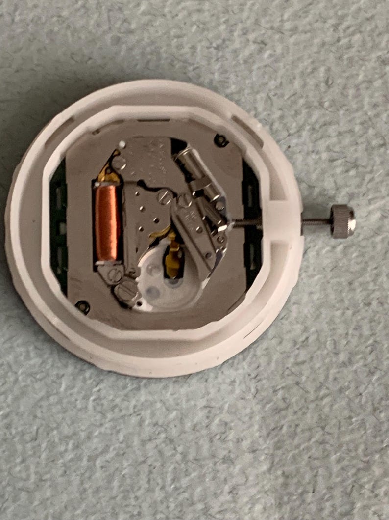 Puede incluir: Un movimiento de reloj con una carcasa de pl&aacute;stico blanco. Los componentes internos incluyen una bobina de color cobre, piezas met&aacute;licas de color plateado y una peque&ntilde;a corona plateada. El mecanismo del reloj est&aacute; dise&ntilde;ado para reparaci&oacute;n o reemplazo.