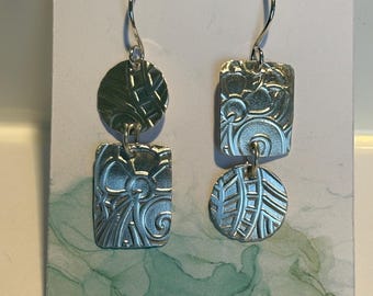 May include: Silver dangle earrings with textured circular and rectangular pendants. The earrings are displayed on a card with the text "Turtle Jewelry Designs.etsy.com" and the brand name "Turtle Jewelry Designs".