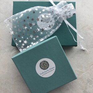 May include: A teal gift box with a white satin ribbon and a white organza bag with silver stars. The box has a sticker with the text "Turtle Jewelry Designs" and the website address "www.TurtleJewelryDesigns.net".