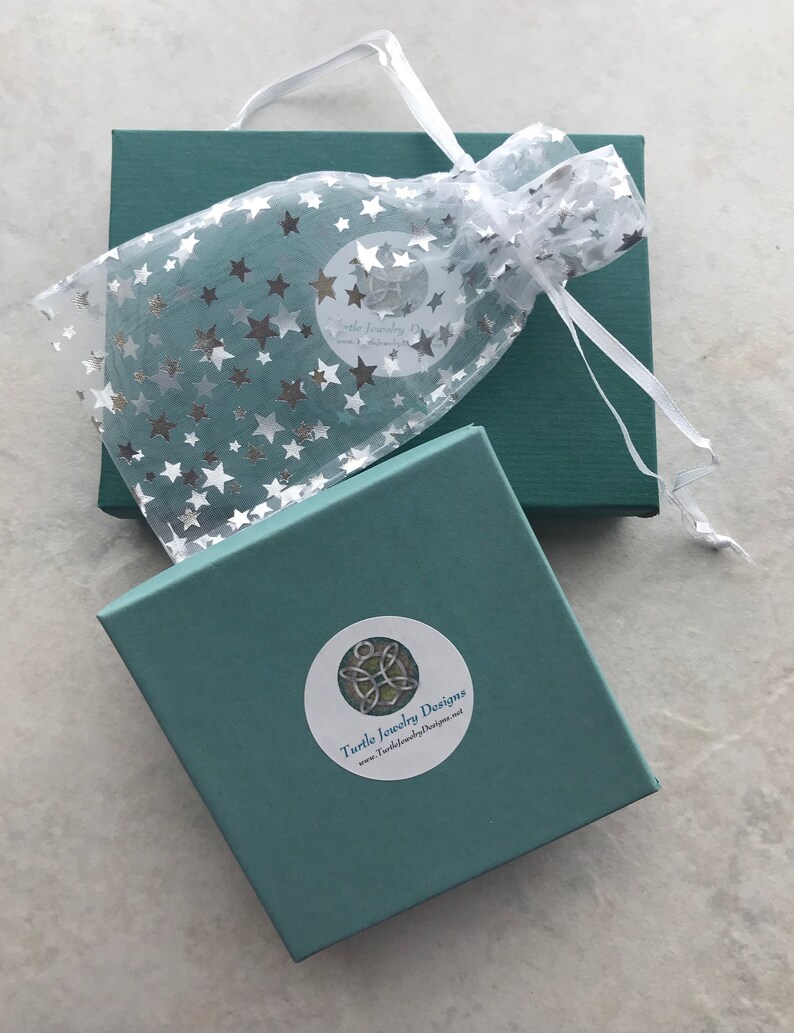 May include: A teal gift box with a white satin ribbon and a white organza bag with silver stars. The box has a sticker with the text "Turtle Jewelry Designs" and the website address "www.TurtleJewelryDesigns.net".