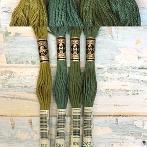 May include: Four spools of DMC embroidery floss in shades of green. The spools are labeled with the DMC numbers 732, 520, 936, and 3362.