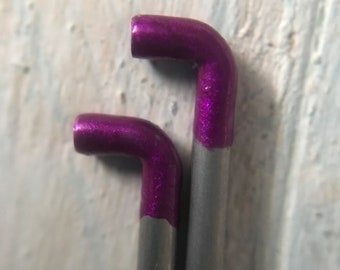Może przedstawiać: Dwie metalowe druty do robótek ręcznych z fioletowymi końcówkami. Druty są srebrne i mają niewielkie zgięcie na górze.