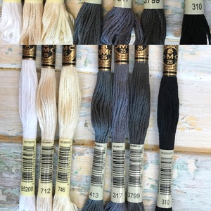 May include: Eight spools of DMC embroidery floss in various colors, including white, cream, gray, dark gray, and black. Each spool has a white label with a barcode, the DMC color number, and the text "DMC" and "25" printed on it.