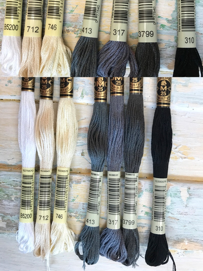 May include: Eight spools of DMC embroidery floss in various colors, including white, cream, gray, dark gray, and black. Each spool has a white label with a barcode, the DMC color number, and the text "DMC" and "25" printed on it.