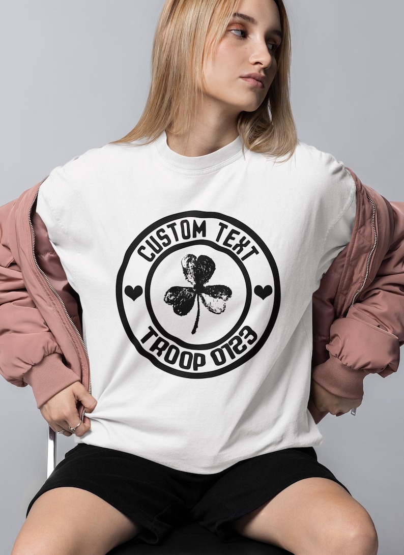 May include: White t-shirt with a black circle design featuring a shamrock, hearts, and the text "CUSTOM TEXT TROOP 0123"