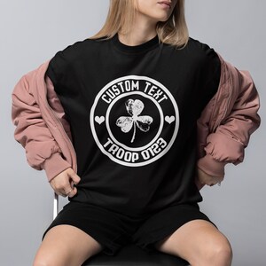 May include: Black t-shirt with a white circle graphic featuring a shamrock, hearts, and the text "CUSTOM TEXT TROOP 0123".