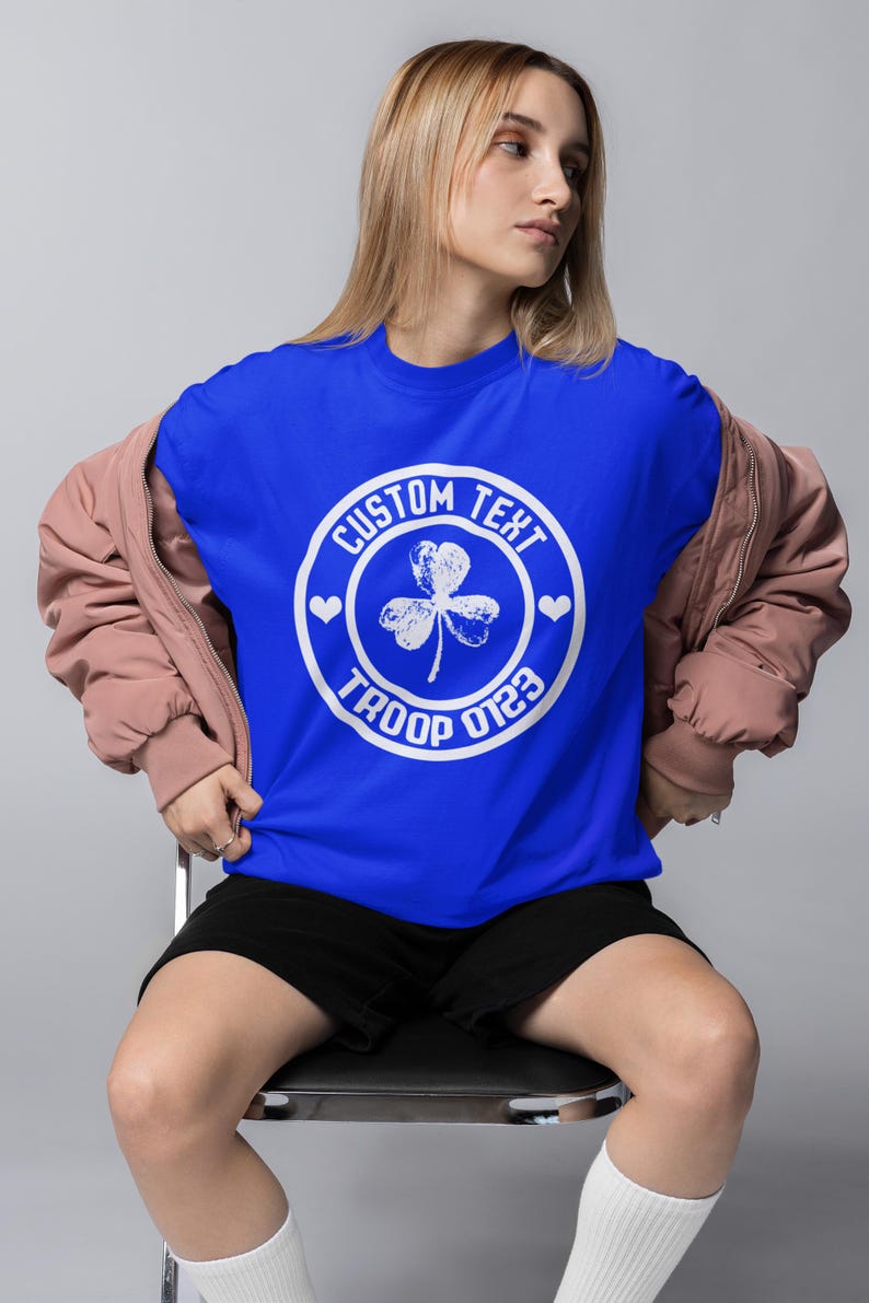 May include: A royal blue t-shirt with a white circle graphic featuring a shamrock, hearts, and the text "CUSTOM TEXT TROOP 0123".