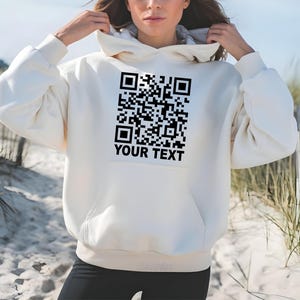 May include: A white hoodie with a black QR code and the text "YOUR TEXT" printed on the front.