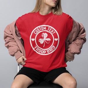 May include: Red t-shirt with a white circle design featuring a shamrock and the text "CUSTOM TEXT TROOP 0123".