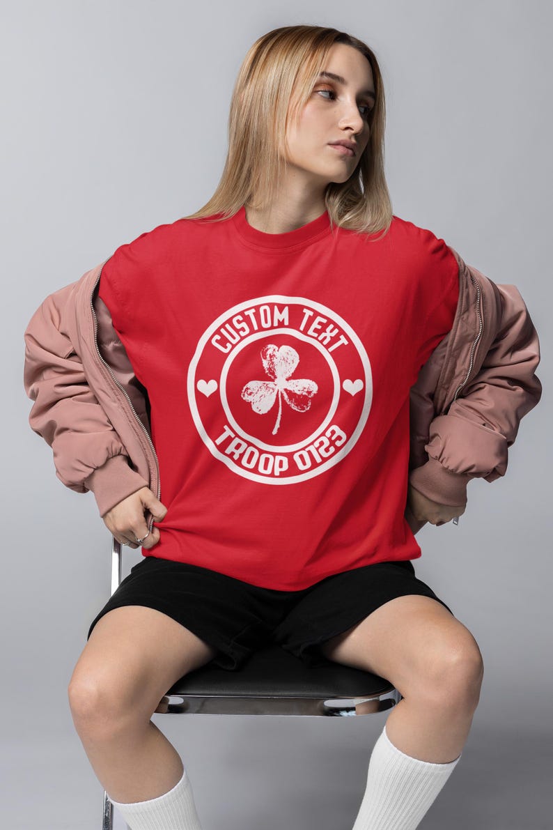 May include: Red t-shirt with a white circle design featuring a shamrock and the text "CUSTOM TEXT TROOP 0123".