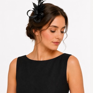 Könnte beinhalten: Ein schwarzer Haarschmuck mit Federn und einer Schleife. Der Haarschmuck wird an der Seite des Kopfes getragen. Die Frau im Bild trägt ein schwarzes ärmelloses Kleid.