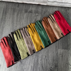 Könnte beinhalten: Eine Sammlung farbenfroher Handschuhe in verschiedenen Farbtönen, darunter Rot, Schwarz, Grün und Gelb. Die Handschuhe sind in einer Reihe angeordnet und zeigen ihre unterschiedlichen Farben und Texturen. Die Handschuhe scheinen aus einem weichen Material zu bestehen, möglicherweise Wildleder oder Leder.