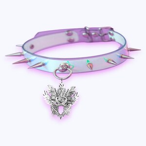 May include: An iridescent choker necklace with silver spikes and a matching pendant. The pendant has a detailed design of wings, an eye, and a floral element. The necklace features a silver ring and clasp.