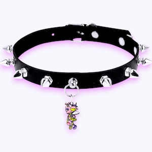 May include: A black collar featuring a series of silver-toned metal spikes along the band and a central silver ring holding a small, colorful cartoon character charm with pink, yellow, and purple details. The collar includes a metal buckle closure.
