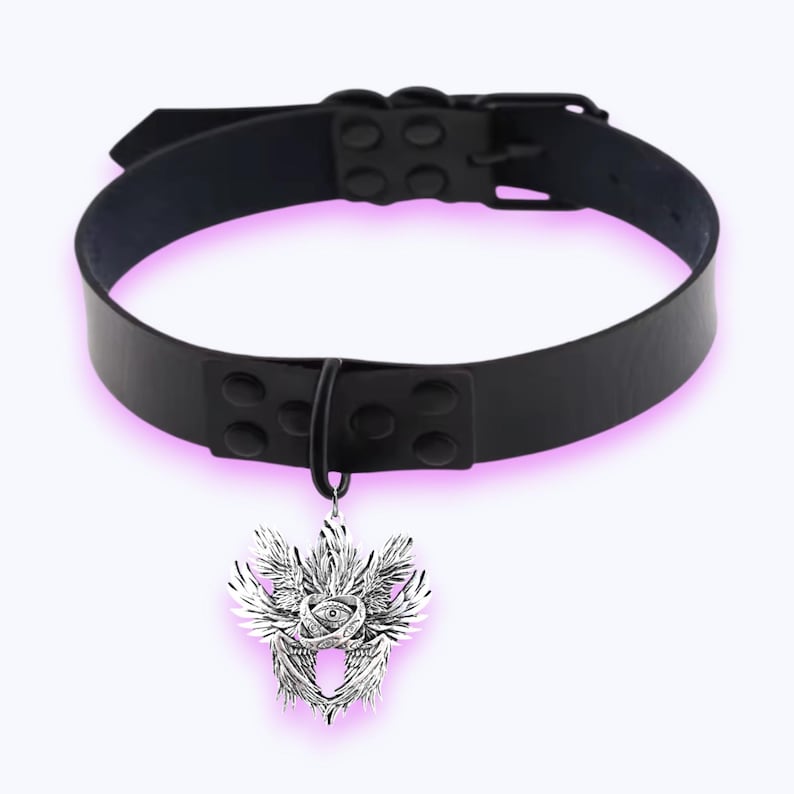 May include: A black choker necklace with a silver pendant. The pendant features a detailed design of wings and an eye. The choker is made of a shiny, black material and has a buckle fastening.