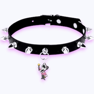 May include: A black collar featuring a series of silver-toned metal spikes arranged around the band. The collar includes a central silver ring holding a small, colorful enamel charm depicting a cartoon character in a pink suit holding a gold staff.