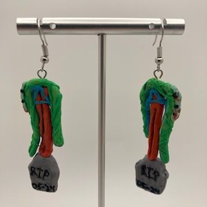 Könnte beinhalten: Ein Paar grüne, orange und blaue Polymer Clay Ohrringe in Form eines Grabsteins mit dem Text "RIP 05-24" auf der Vorderseite. Die Ohrringe hängen an silbernen Haken.