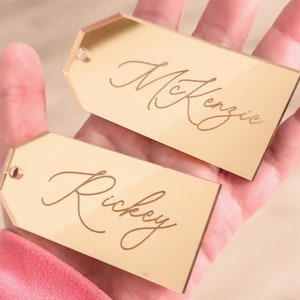 May include: Two gold mirror-like gift tags with the names "Kenzie" and "Rickey" written in cursive.