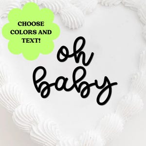 Op de afbeelding: Een witte taart met witte glazuur en de woorden "oh baby" in zwart schrift. Een groene, geschulpte vorm met de tekst "CHOOSE COLORS AND TEXT!" staat in de linkerbovenhoek. De taart is versierd met witte glazuur.