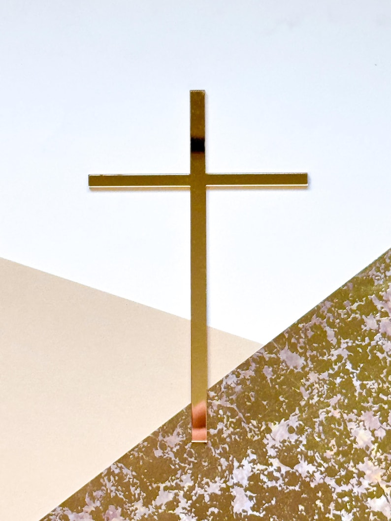 May include: A gold metal cross with a simple design. The cross is on a white and beige background.