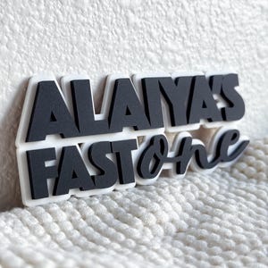 May include: Black and white sign with the text "Alaiya's Fast & Furious" in a bold, stylized font.
