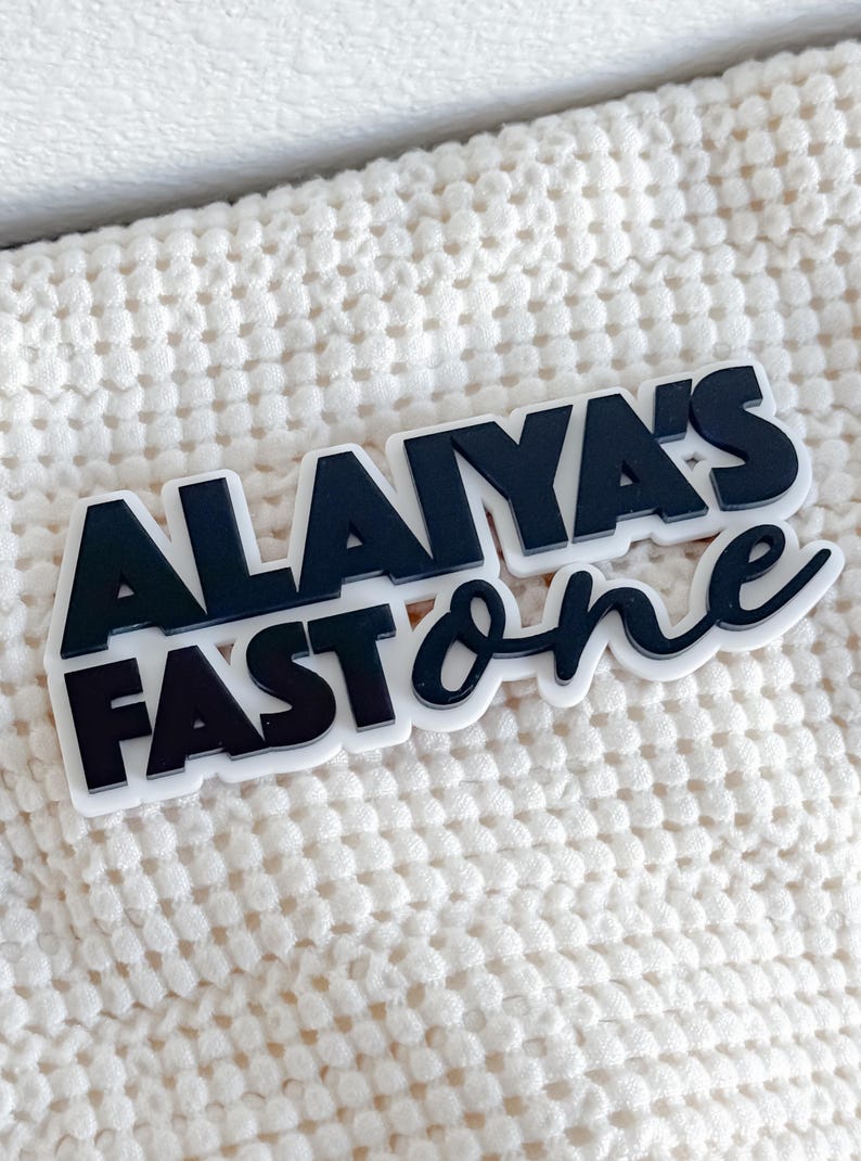 May include: Black and white plastic sign with the text "Alaiya's Fast One" in a bold, stylized font.