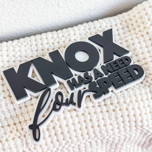May include: Black and white decorative sign with the text "Knox has a need for speed".