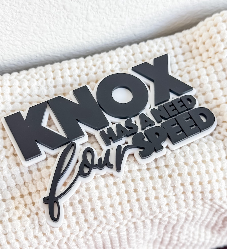 May include: Black and white decorative sign with the text "Knox has a need for speed".