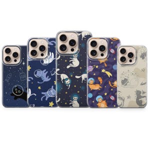 May include: A collection of five phone cases with space-themed cat designs. The cases feature various dark blue and beige backgrounds with illustrations of cats in astronaut helmets, planets, stars, and other space elements.