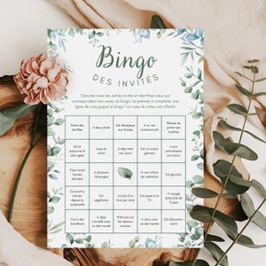 Peut inclure: Une carte de jeu de Bingo imprimée avec une bordure florale et le titre "Bingo des Invités". La carte présente une grille de cases avec diverses invites. Une fleur rose et de la verdure sont en arrière-plan.