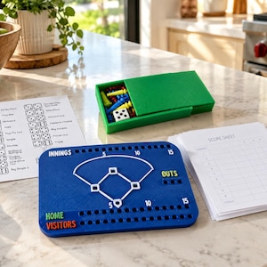 May include: A blue baseball board game with a white diamond field, score tracking holes, and labels for innings, outs, home, and visitors. Includes a green storage box with colorful pegs and a die, a white reference card, and a stack of score sheets.
