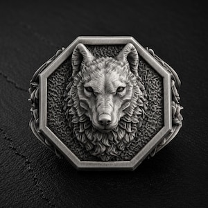 May include: A silver-toned ring featuring a detailed, three-dimensional wolf head relief centered within an octagonal frame. The metal surface has a brushed, oxidized finish with intricate fur textures and a decorative border of leaf-like motifs.