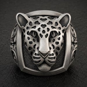 May include: A silver-toned ring featuring a sculpted leopard head as the centerpiece. The leopard design includes detailed spots and facial features with a brushed metal finish. The sides of the ring band display intricate, carved scrollwork patterns.