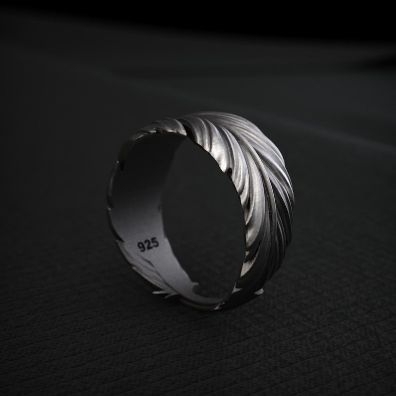 K&ouml;nnte beinhalten: Ein silberner Ring mit einem strukturierten Federdesign. Der Ring besteht aus 925er Sterlingsilber und hat eine polierte Oberfl&auml;che. Der Ring ist ein breites Band und eignet sich f&uuml;r den t&auml;glichen Gebrauch.