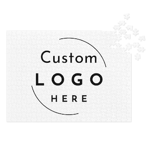 May include: A white jigsaw puzzle with the words "Custom LOGO HERE" in black, encircled by a black arc. Some puzzle pieces are separate. The puzzle is rectangular.