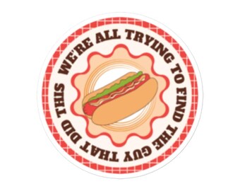 Può includere: Un adesivo circolare rosso e bianco con il testo "We're all trying to find the guy that did this" in un carattere marrone. Un hot dog di cartone animato con senape e relish è al centro dell'adesivo.